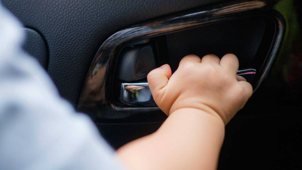 18 months / 1 year old baby boy child holding on to the door handle inside of the car, kid try to open the car door, Child safety concept