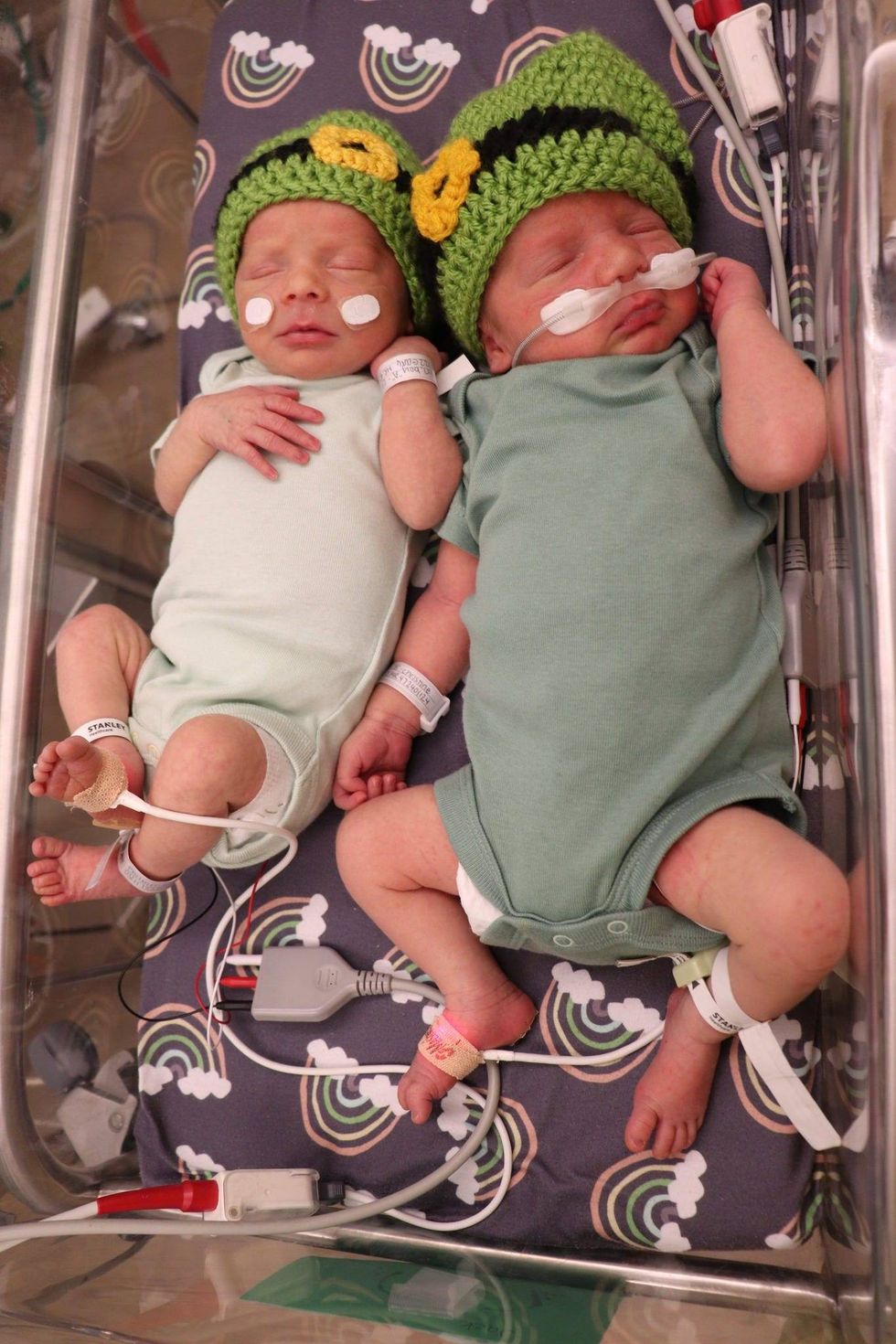 2 newborns, wearing green and leprechaun hats share a bassinet