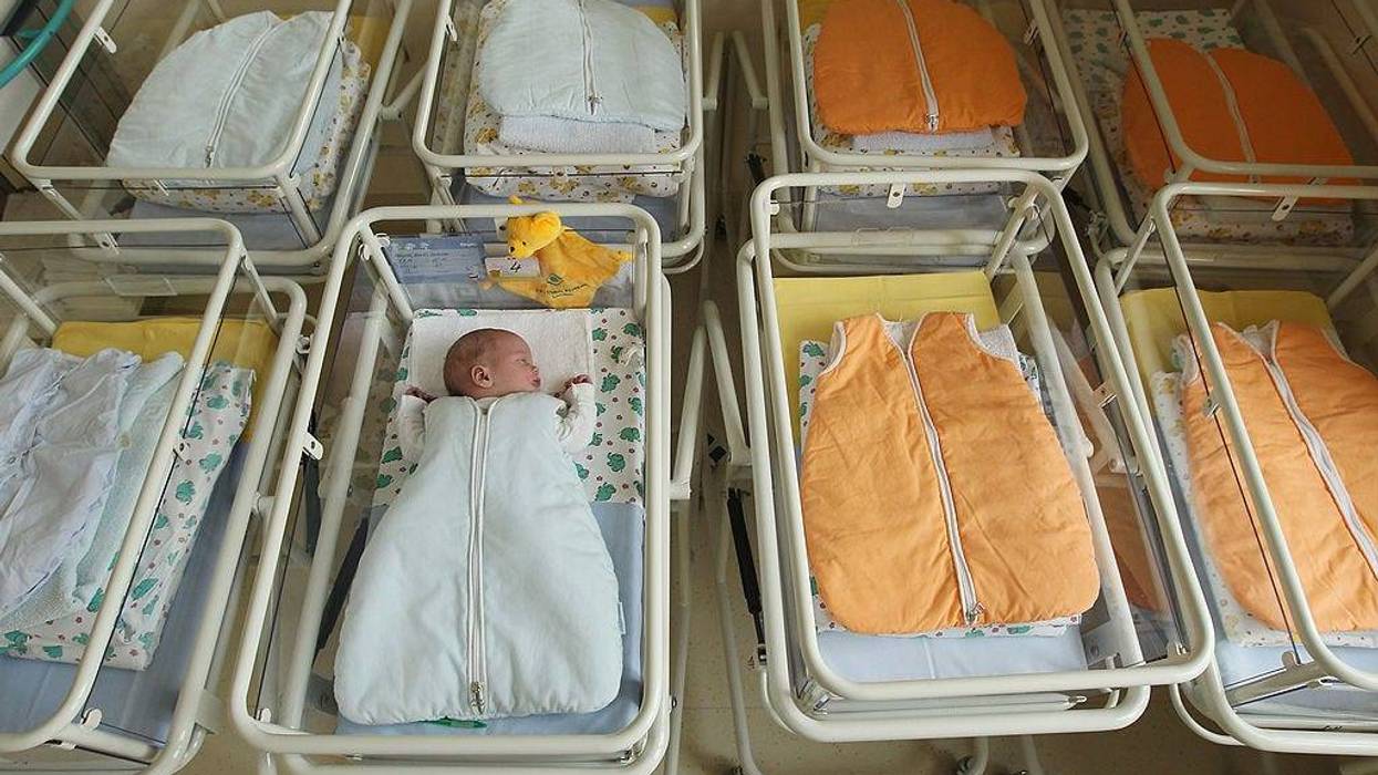 A 4-day-old newborn baby, who has been placed among empty baby beds by the photographer, lies in a baby bed in the maternity ward of a hospital.