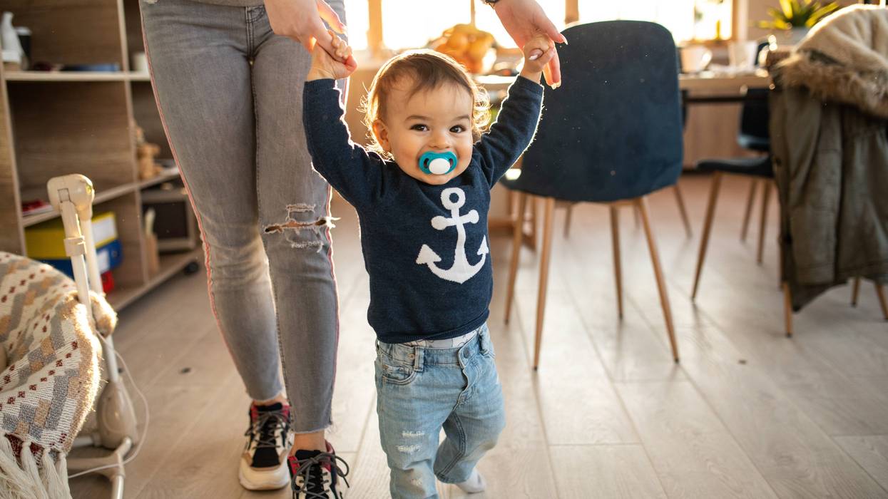 A baby walking, holding hands with a woman.