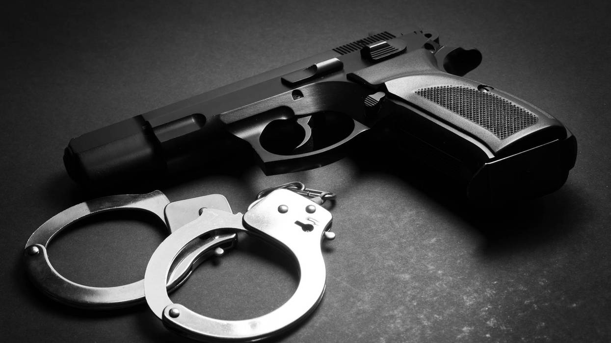 A black handgun and silver handcuffs on a dark surface, in black and white.