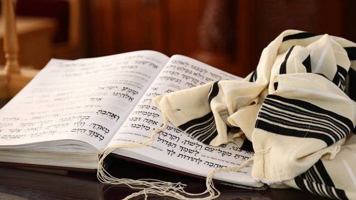 A book of Jewish scripture and a prayer shawl sit on a table.