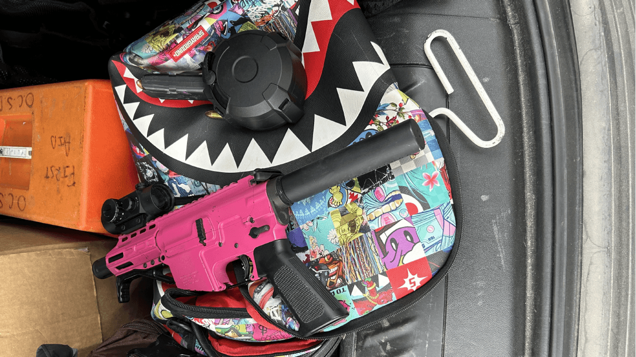 A bright, and colorful backpack featuring dozens of different pictures has a pink handgun resting on top of it.