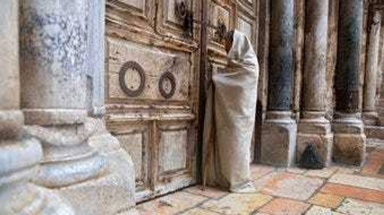 A Christian worshiper stands at the closed door of the Church of the Holy Sepulchre, believed by many Christians to be the site of the crucifixion and burial of Jesus Christ, in Jerusalem, Friday, April 10, 2020. (AP Photo/Sebastian Scheiner)