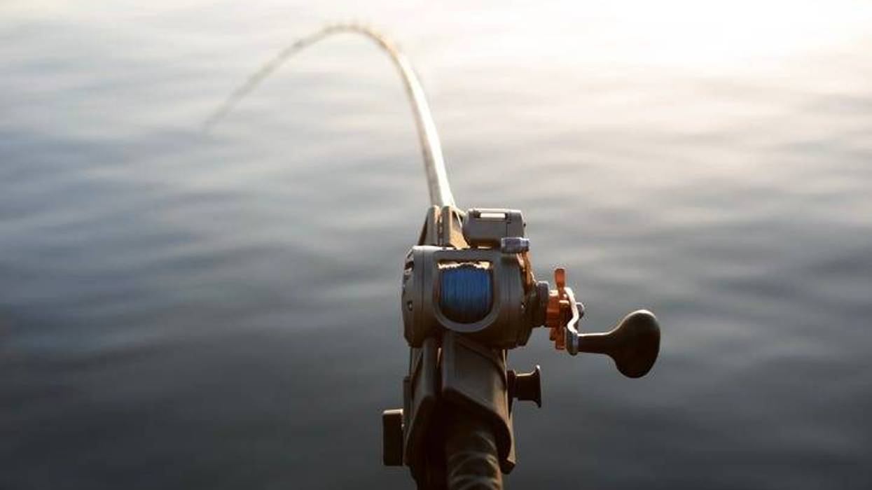 A close-up photo of a fishing rod and reel during a summer fishing trip. The background shows calm, out-of-focus water.