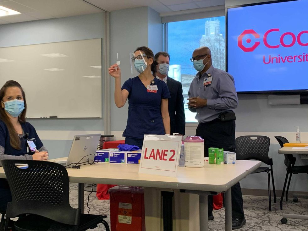 A Cooper nurse holds up a vial of the COVID-19 vaccine, as the third in line to get then shot, Dr. Guy Hewlett, stands by.