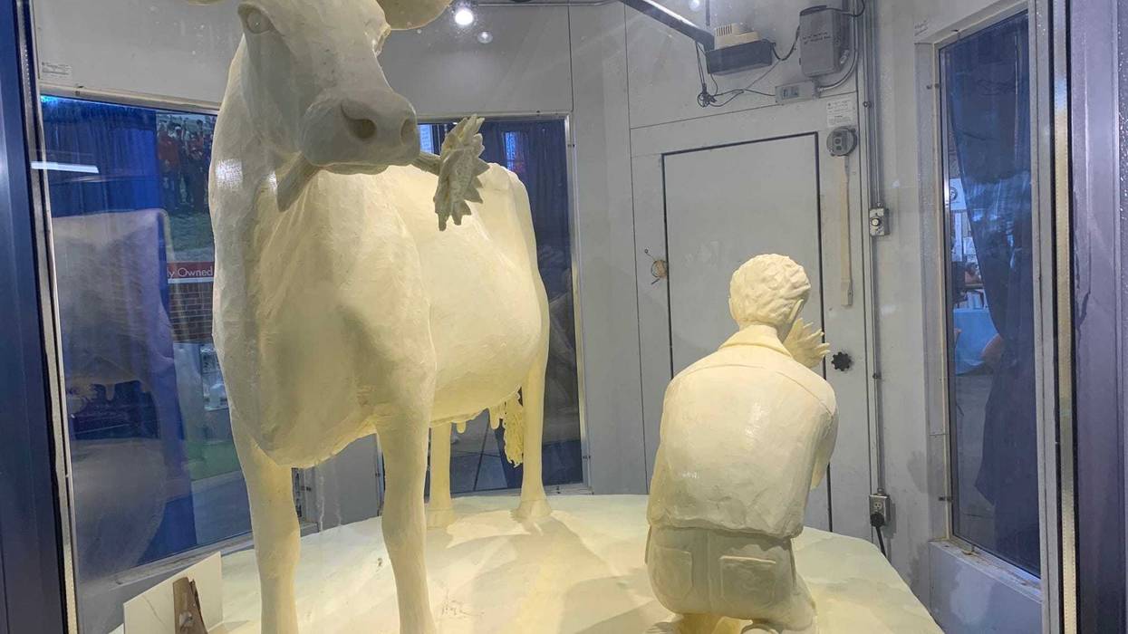 A cow holding a sunflower stands next to a farmer -- all made of butter.