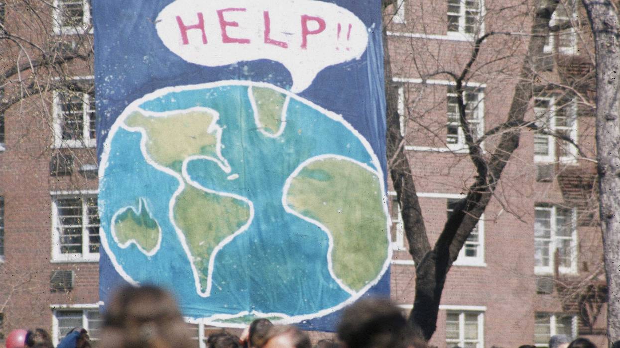 A crowd of people gather near a large poster that shows a speach bubble from planet Earth that reads 'Help!!', on the occaision of the first Earth Day conservation awareness celebration, New York, New York, April 22, 1970.