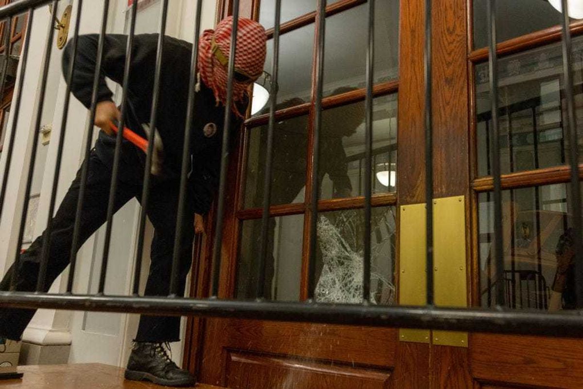 A demonstrator breaks the windows of the front door of the building in order to secure a chain around it to prevent authorities from entering on Tuesday, April 30, 2024 in New York City.