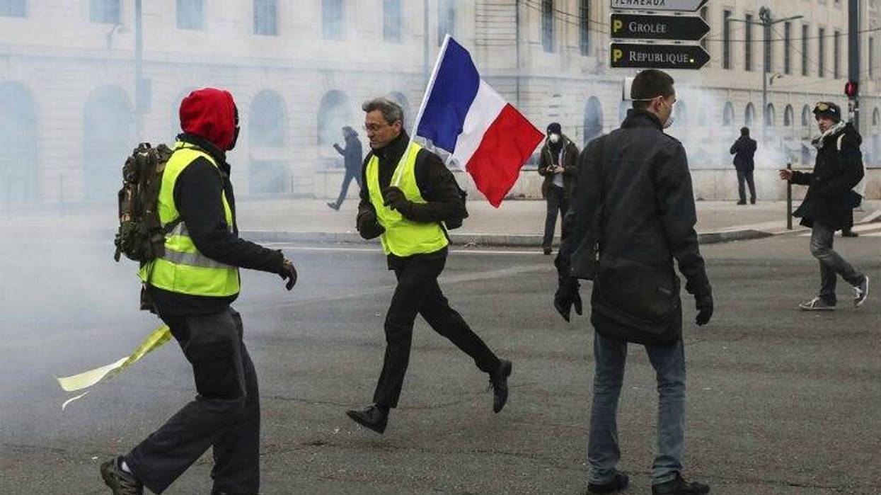 A demonstrator carries a French flag as yellow vest demonstrators are hit by tear gas during clashes in Lyon, central France, Saturday, Jan. 26, 2019.