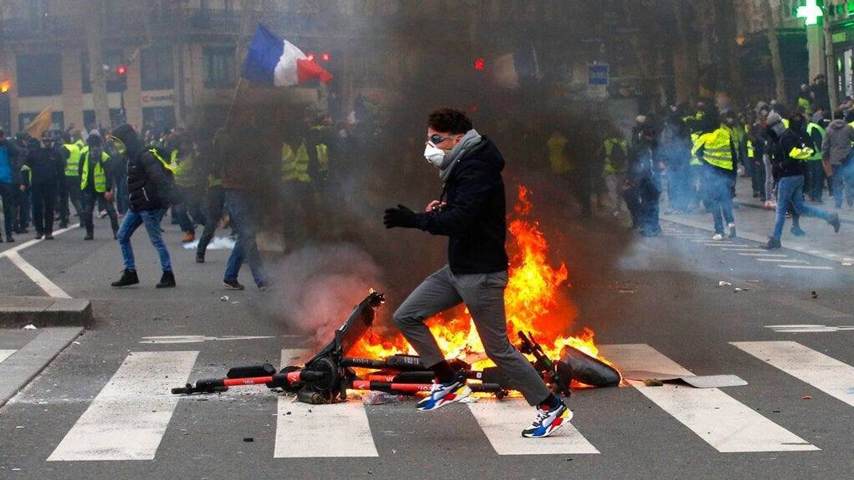 A demonstrator runs by a fire during a yellow vest protest Saturday, Feb. 2, 2019 in Paris