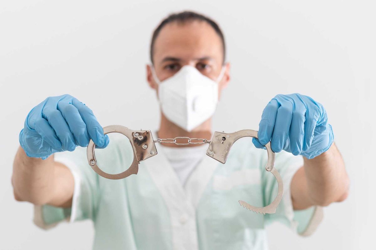 A doctor in a protective medical suit with handcuffs in his hands