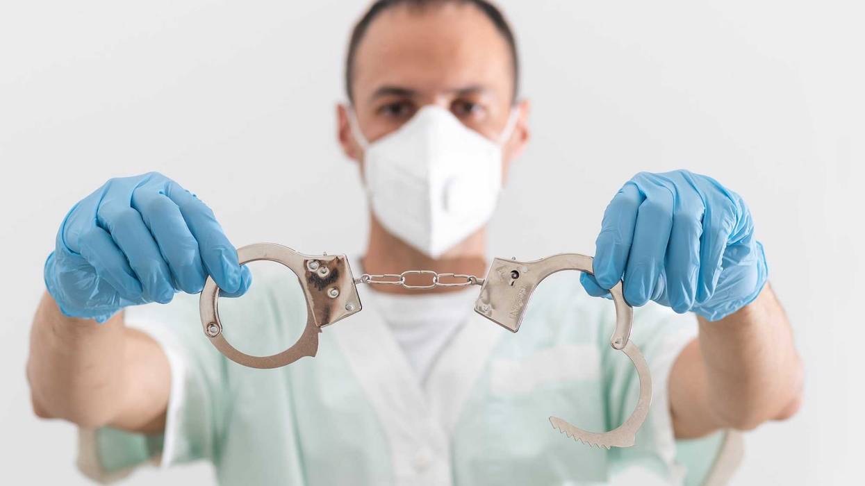 A doctor in a protective medical suit with handcuffs in his hands