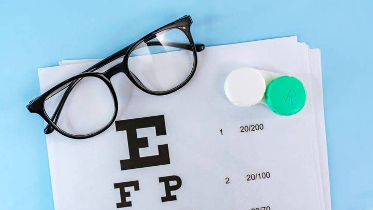 A doctor poster for visual acuity testing and glasses with a container for contact lenses on a blue table.