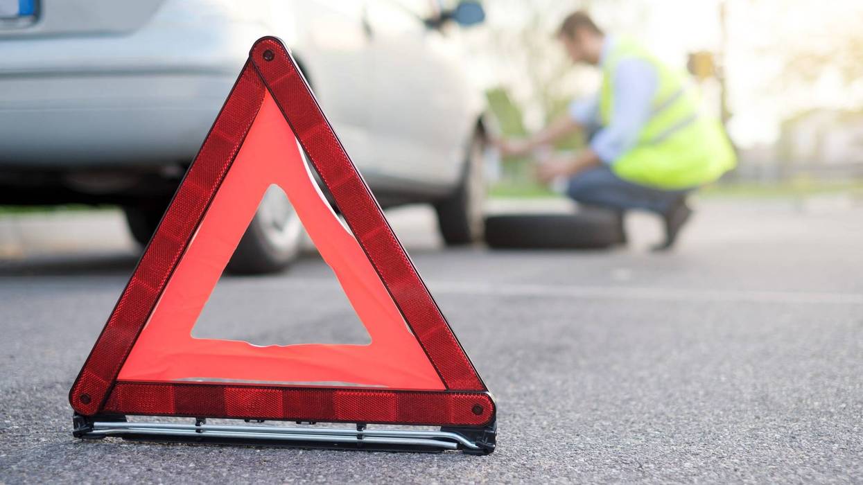 A driver changes a tire on the side of the road.