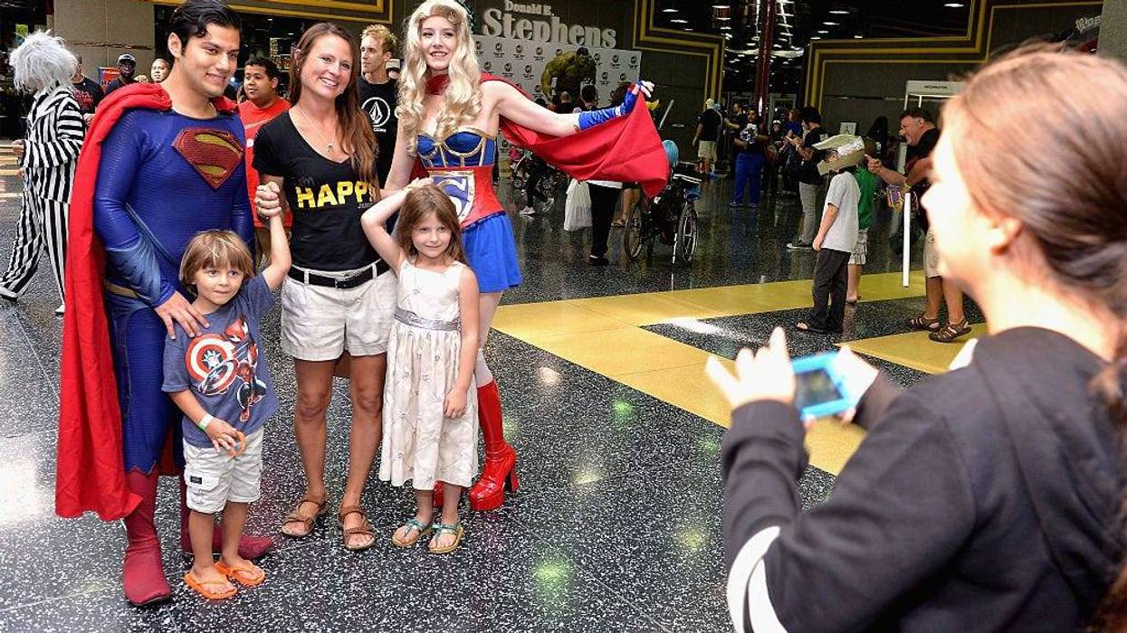 A family posing with people dressed as Superman and Supergirl