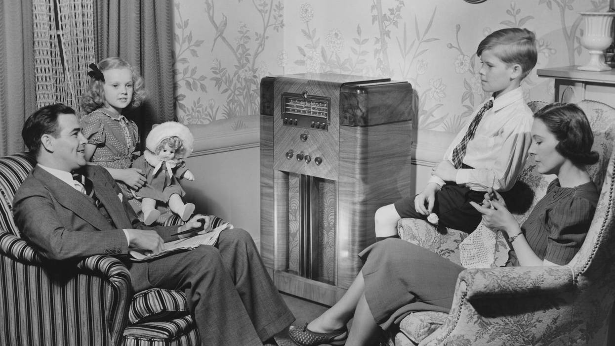 A family sits around a large radio set in the early 20th Century