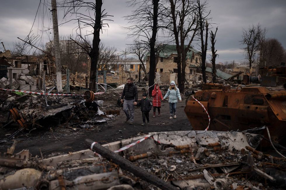 A family walks amid destroyed Russian tanks in Bucha, on the outskirts of Kyiv, Ukraine, Wednesday, April 6, 2022.