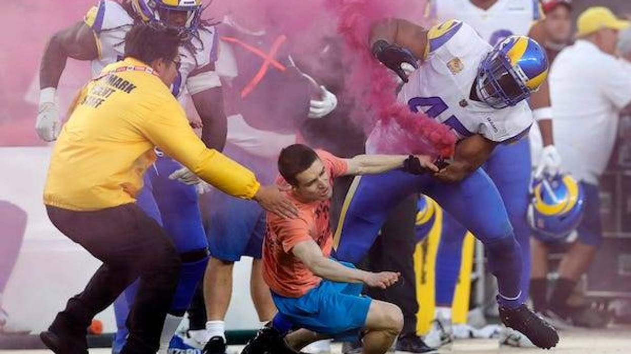 A fan with a smoke bomb is tackled on the field by Los Angeles Rams' Bobby Wagner