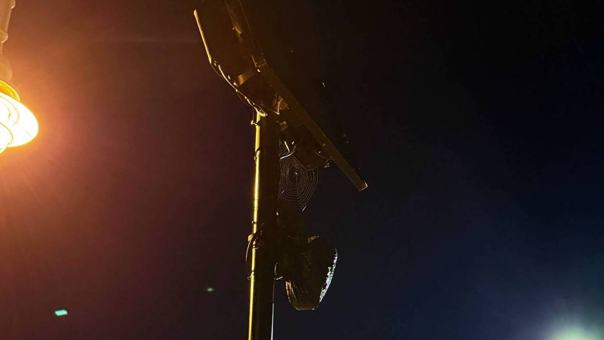 A flock camera covered by a dark plastic bag illuminated by a warm street light on a dark night.