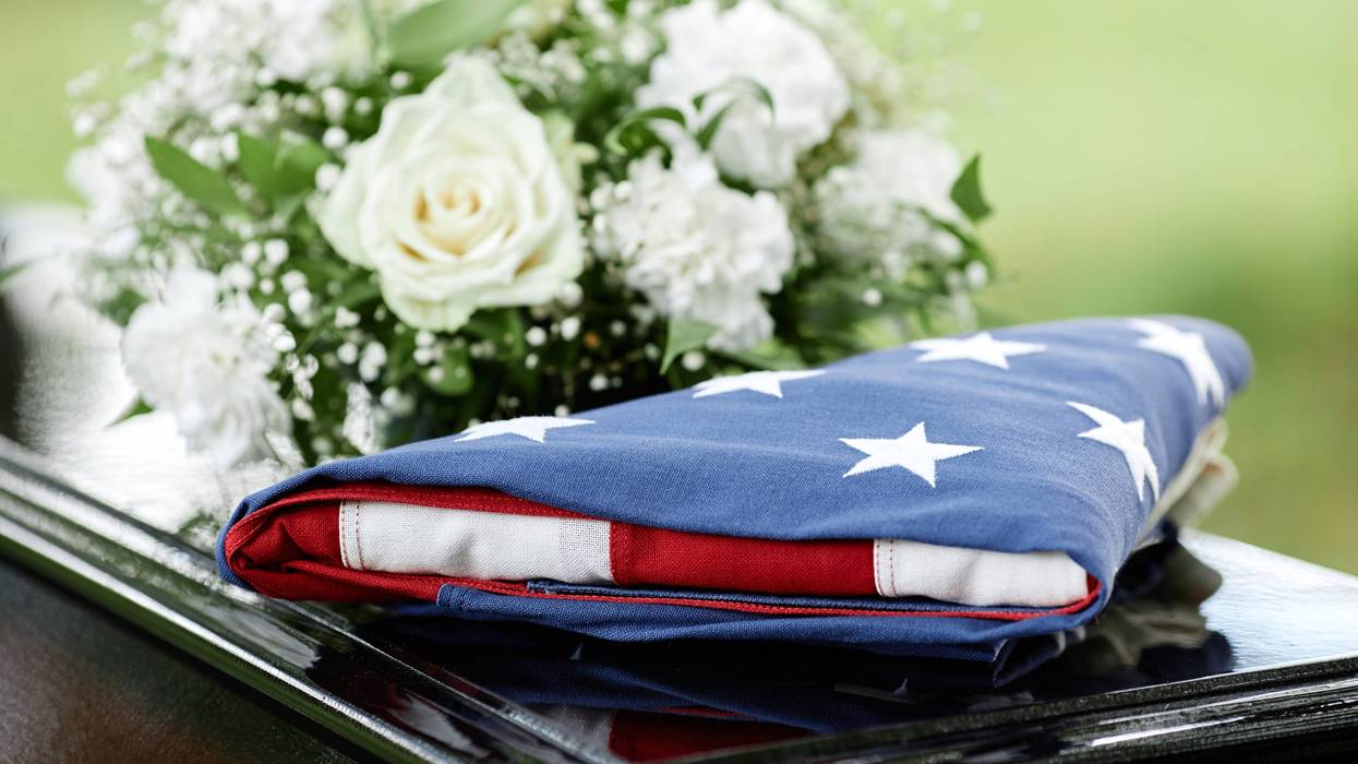 A folded American flag and flowers on top of a casket.