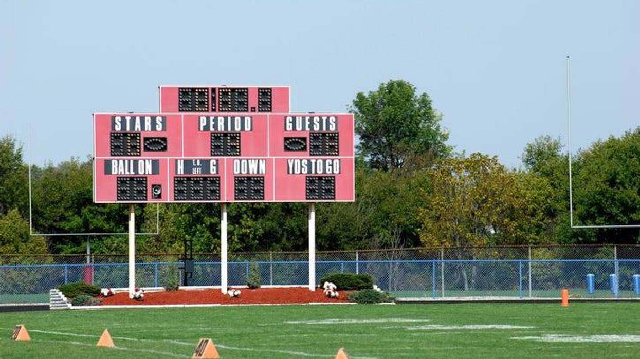 A football field. Focus is on the scoreboard. The cross posts are visible in the background.