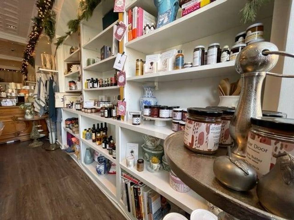 A giant open kitchen overlooks cozy wooden tables and tan, puffy pillows underneath soft lit chandeliers. There is retail from local artists and cheeses and charcuterie from Illinois growers in front.