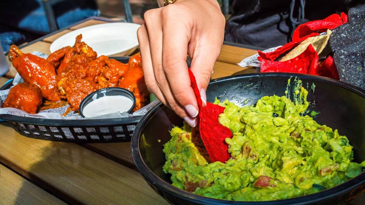 A girl dips into the guacamole with chips along with buffalo wings on the side as appetizers.