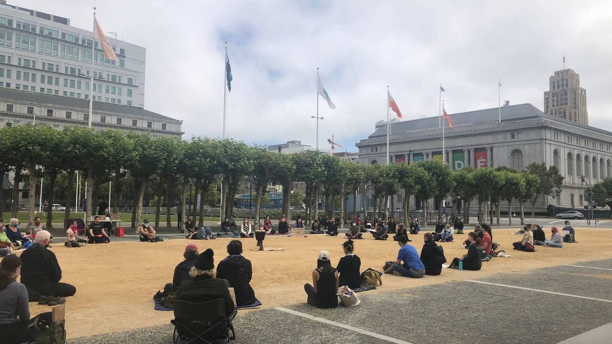 A group of about 100 people sits and meditates in front of City Hall in San Francisco.