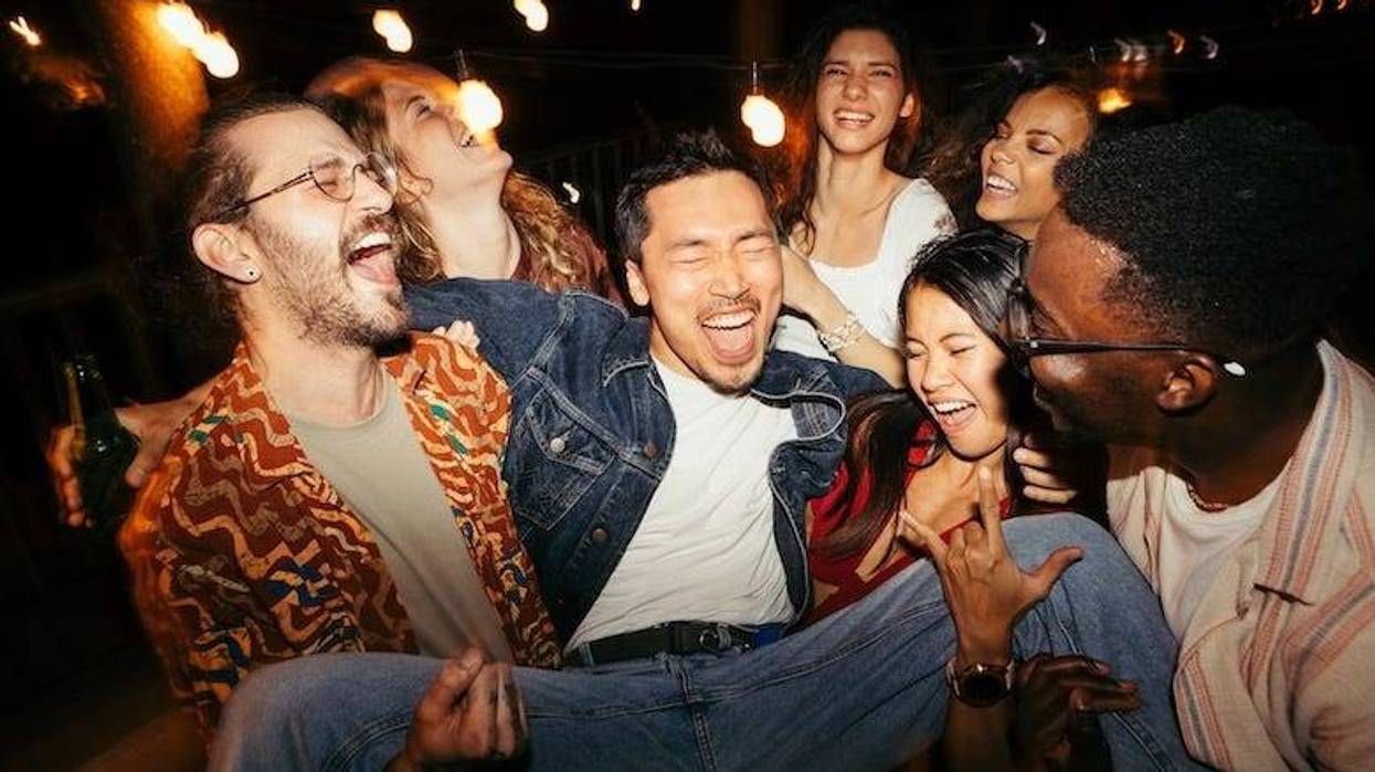 A group of friends lifting their male tipsy friend at a rooftop night outdoor party