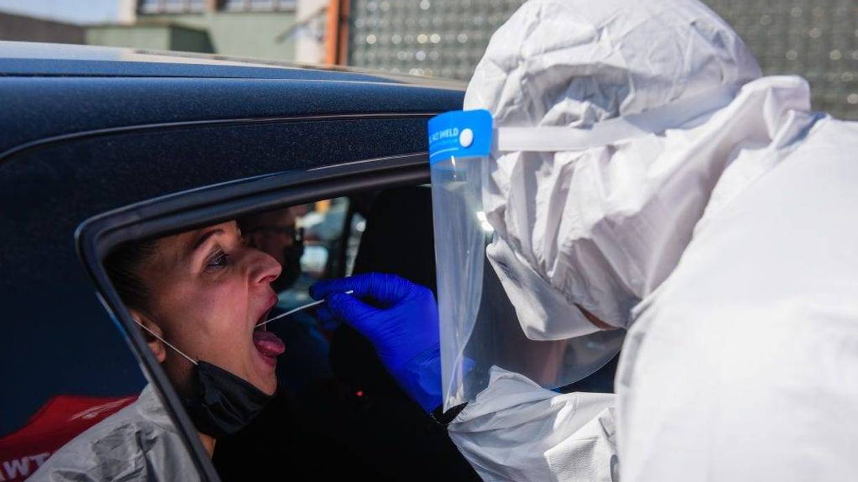 A health worker wears a protective suit, gloves, mask and a face shield as she takes a saliva sample