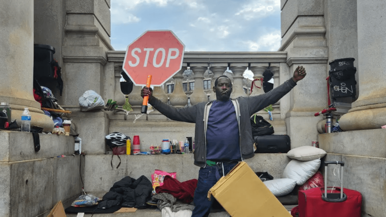 A homeless man defiantly raises a stop sign after police and sanitation workers force him to dismantle his makeshift tarp shelter at the base of the Manhattan bridge on Sept. 22, 2022.
