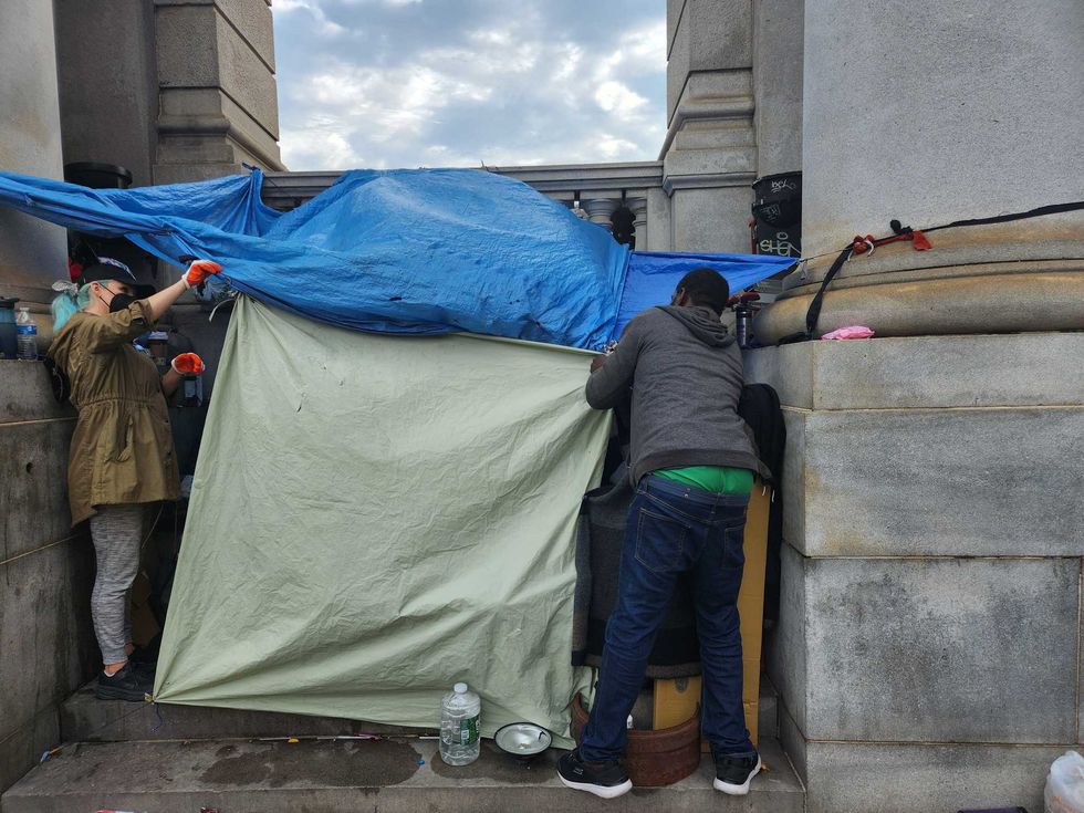 A homeless man works with a volunteer to dismantle the shelter he was living in as police and sanitation workers gather.
