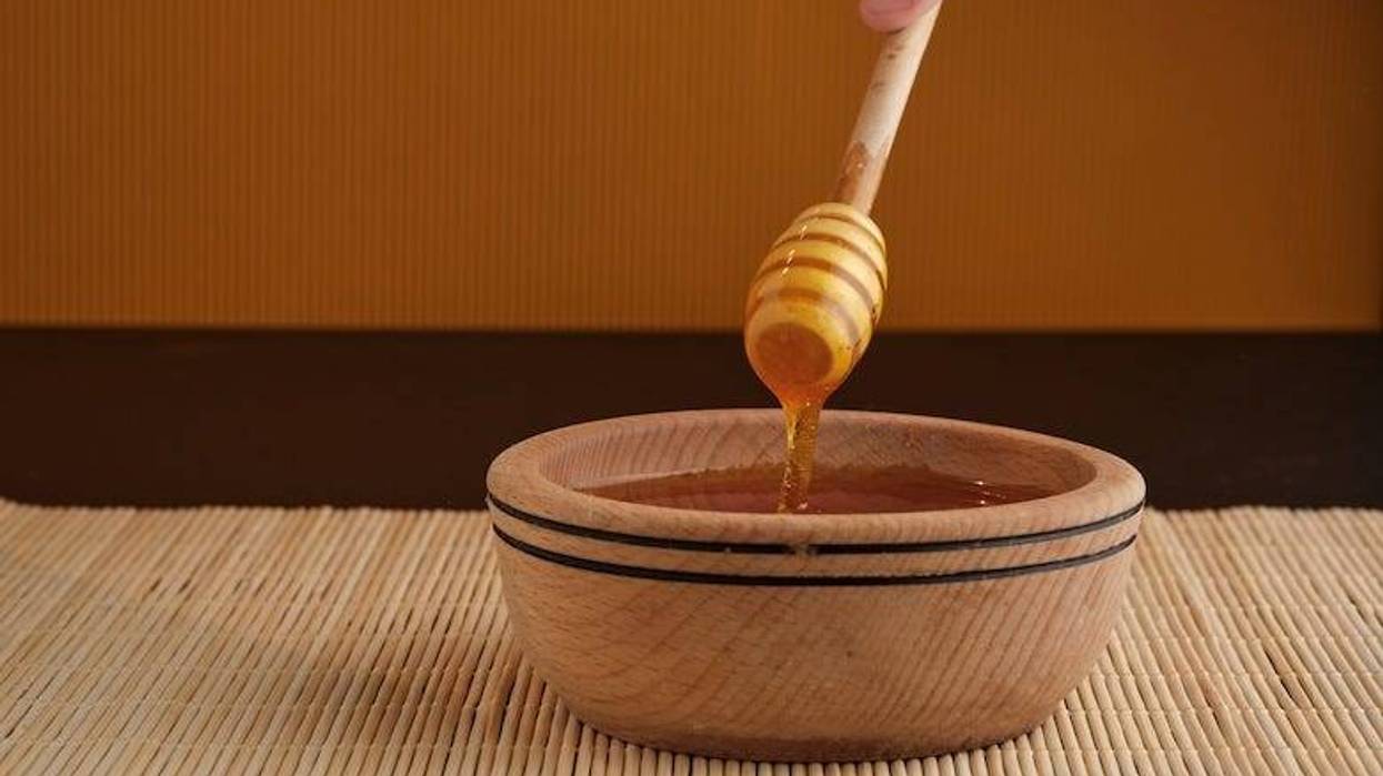 A honey stick dipper being dipped into a wooden bowl