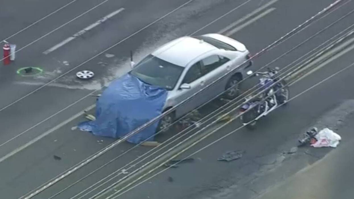 A light-colored sedan with a blue tarp over its hood and tire rim broken off