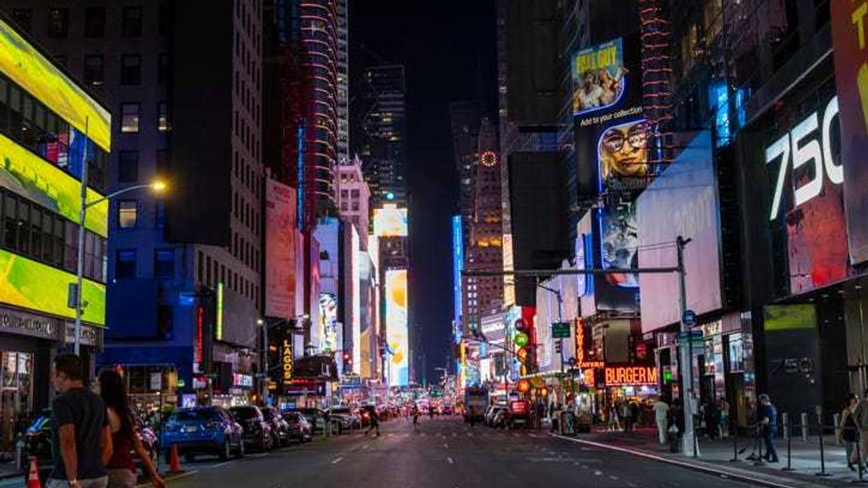 A lively crowd fills the streets of Times Square, surrounded by bright, colorful billboards that light up the night sky, creating an energetic atmosphere.