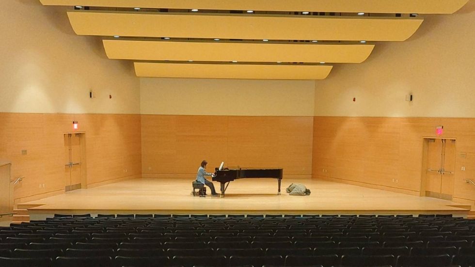 A lone pianist practices on a Steinway & Sons piano on stage inside CMS Concert Hall.