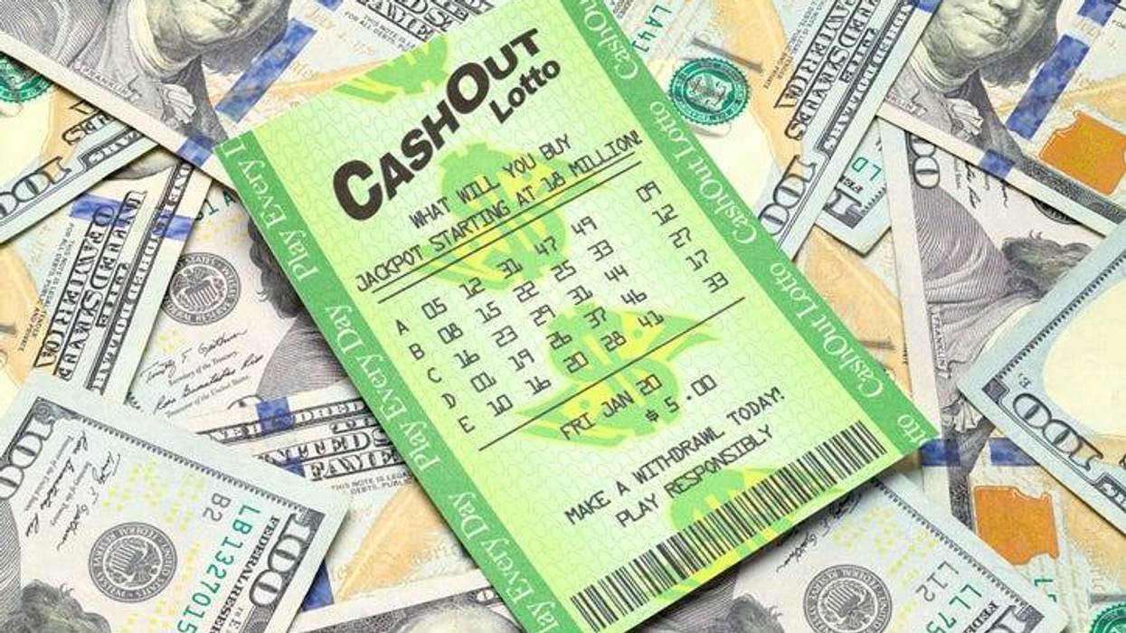 A lottery ticket sits on top of a pile of scattered one hundred dollar bills.