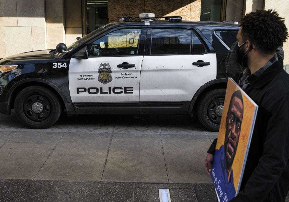 A man carrying a portrait of George Floyd looks on at a police cruiser as demonstrators march in honor of George Floyd on March 7, 2021 in Minneapolis, Minnesota.