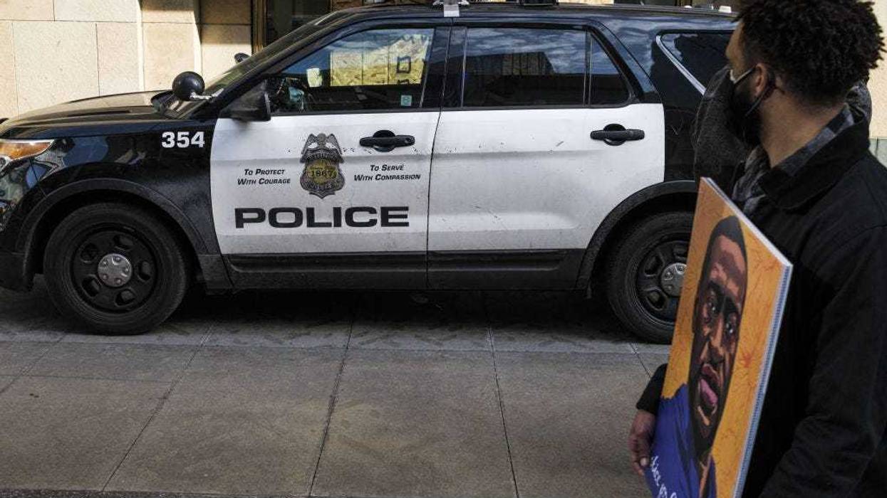 A man carrying a portrait of George Floyd looks on at a police cruiser as demonstrators march in honor of George Floyd on March 7, 2021 in Minneapolis, Minnesota.