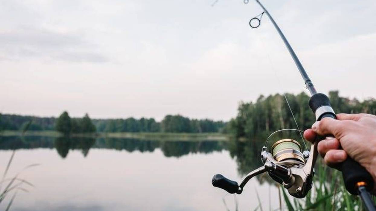 A man casting a line to fish in a lake surrounded by trees.