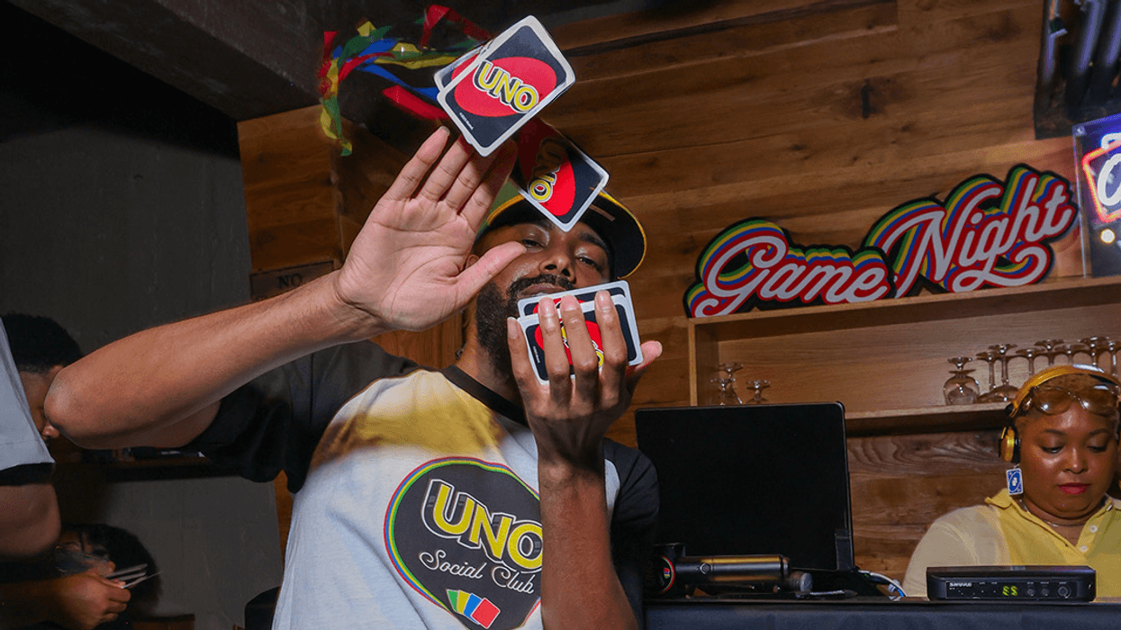 A man flips UNO cards while a DJ spins behind him.