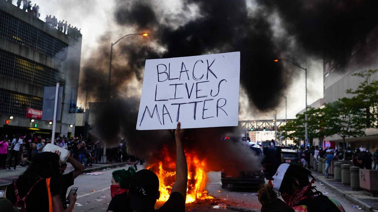 A man holds a Black Lives Matter sign as a police car burns during a protest on May 29, 2020 in Atlanta, Georgia.