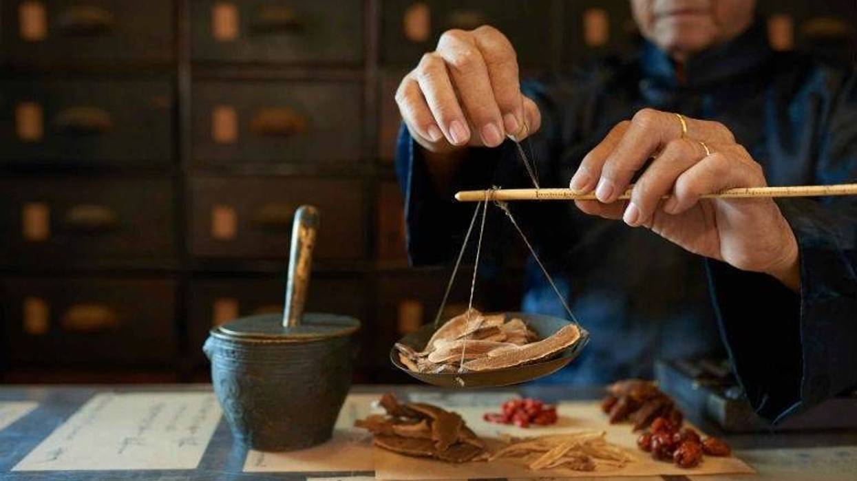 A man measures ingredients in traditional Asian apothecary.