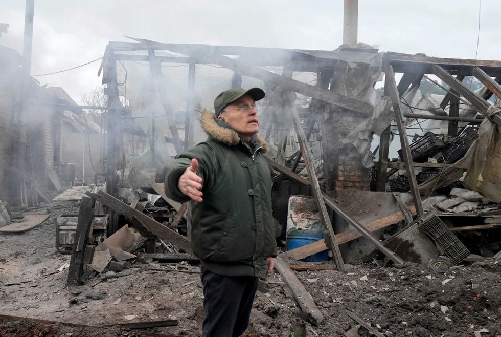 A man opens his arms as he stands near a house destroyed in the Russian artillery shelling, in the village of Horenka close to Kyiv, Ukraine, Sunday, March 6, 2022