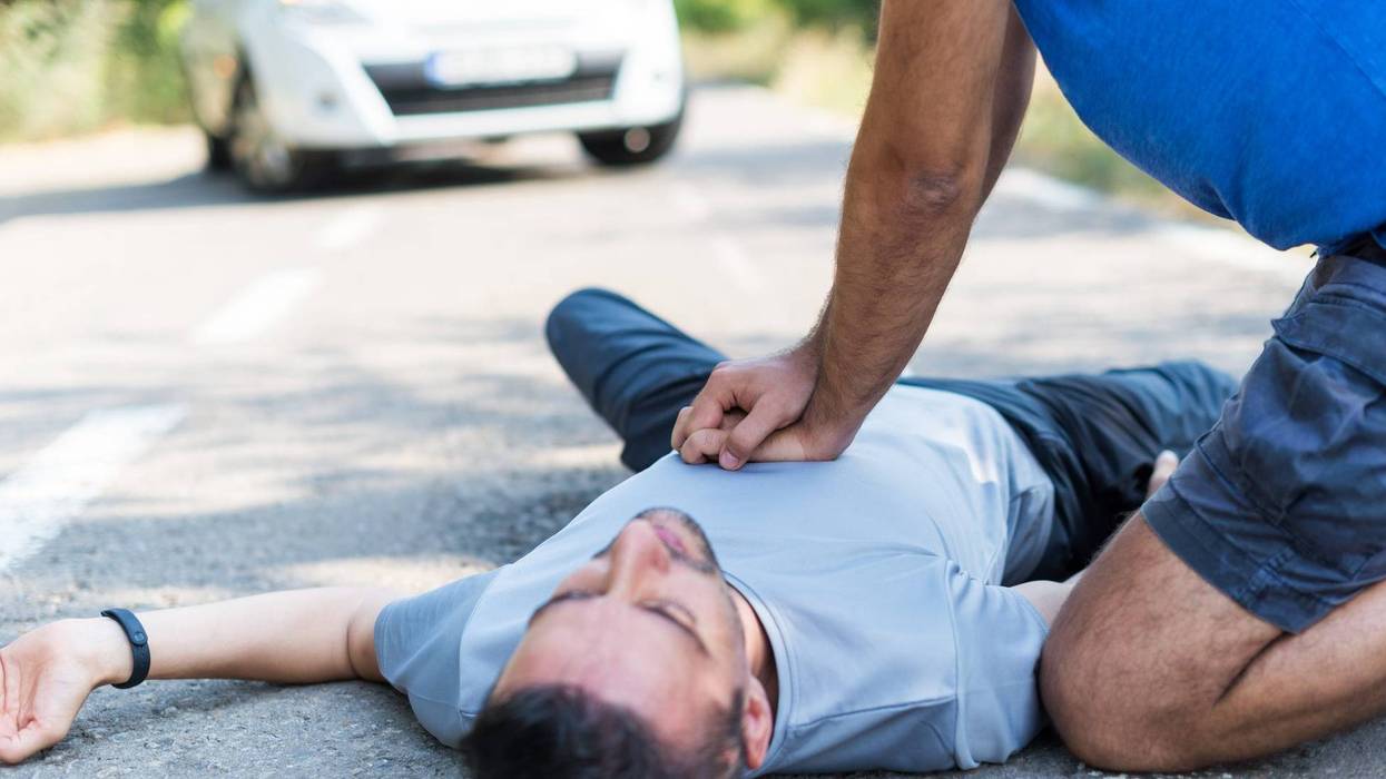 A man performs CPR on a another man laying on the ground
