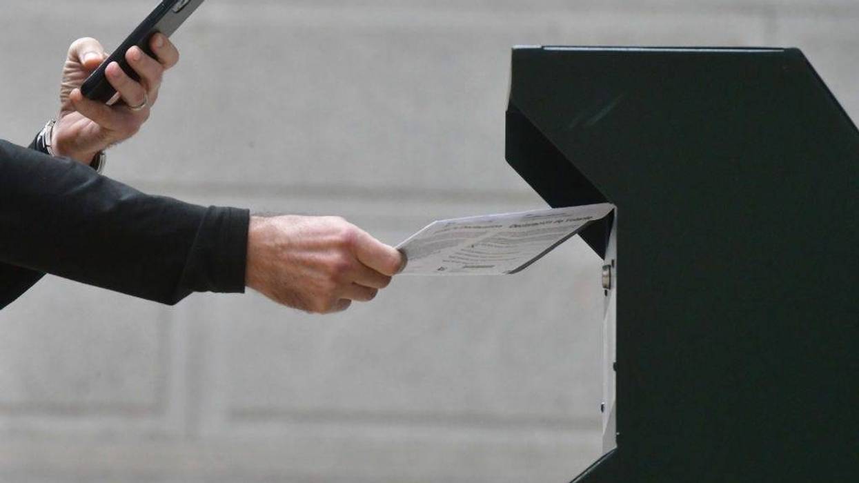 A man photographs himself depositing his ballot in an official ballot drop box while a long line of voters queues outside of Philadelphia City Hall at the satellite polling station on October 27, 2020, in Philadelphia, Pennsylvania.