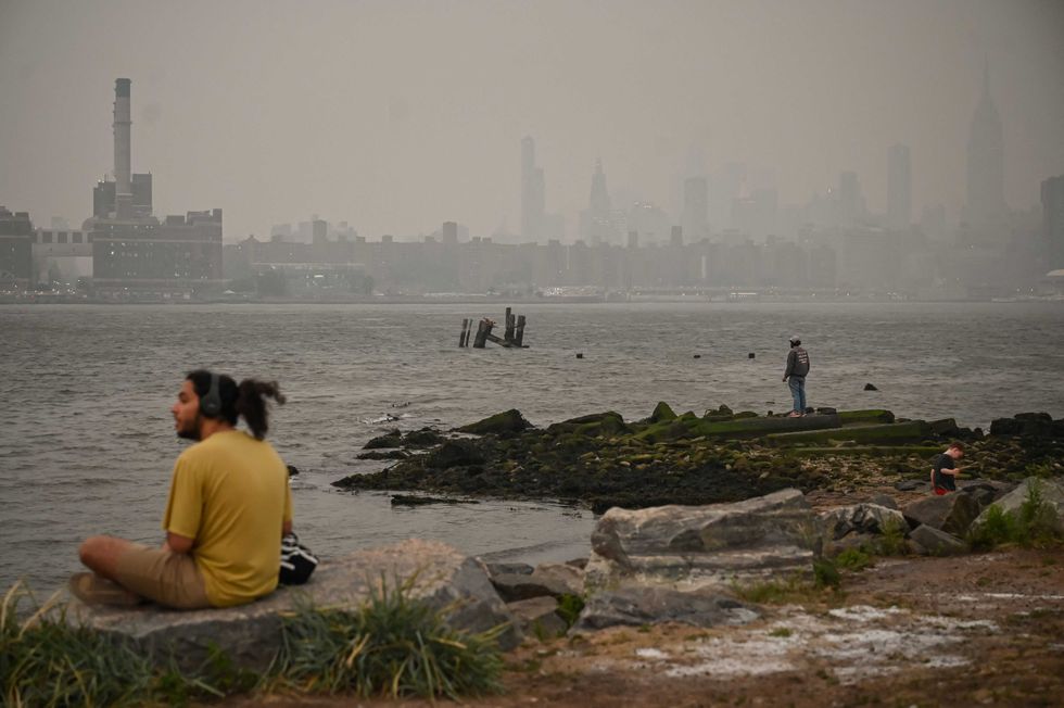 A man sits along the East River as New York City is shrouded in smoke on June 6, 2023
