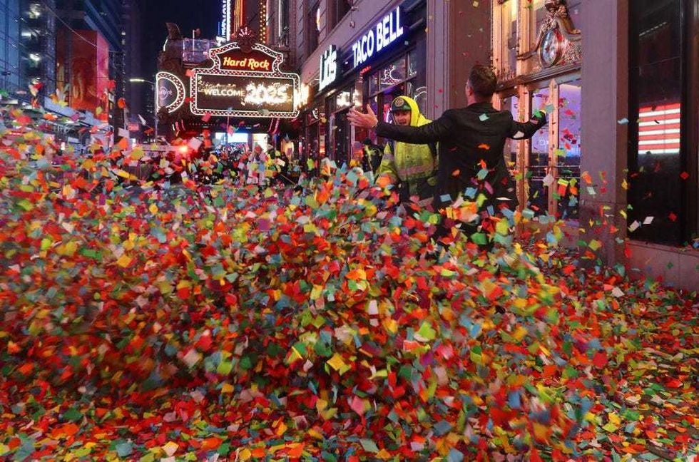 A man stands on a sidewalk filled with confetti as Dept. of Sanitation workers begin the cleanup following New Year