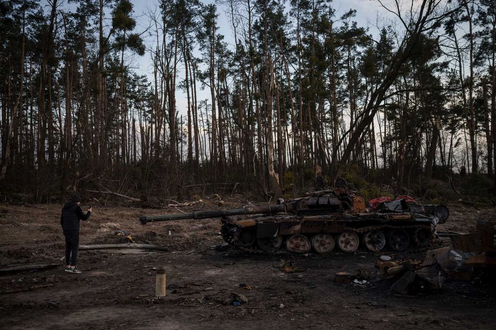 A man takes photos of a destroyed tank near Kyiv, Ukraine, Monday, April 4, 2022